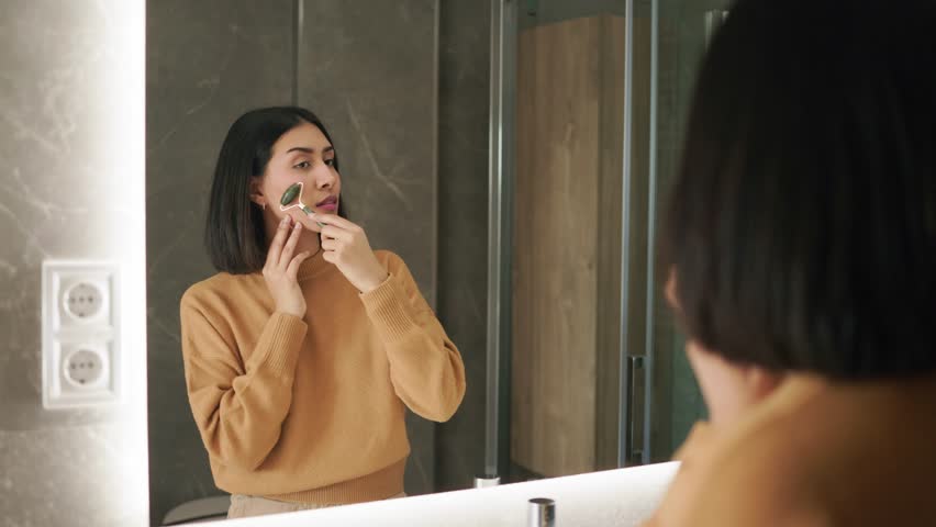 Woman performing a self care beauty routine with a facial roller in the bathroom