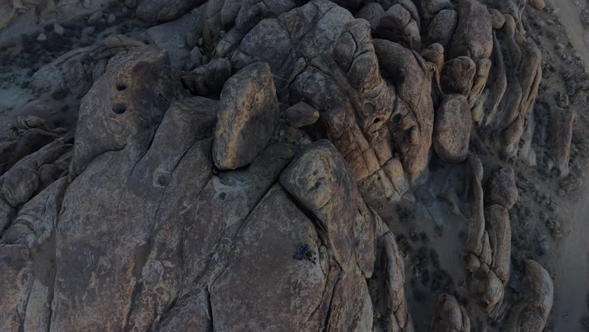 Horizontal 4K real-time drone video in Alabama Hills, California, ascending from above a person sitting on a boulder, revealing the expansive desert landscape, rock formations, and distant Eastern Sierra mountains.