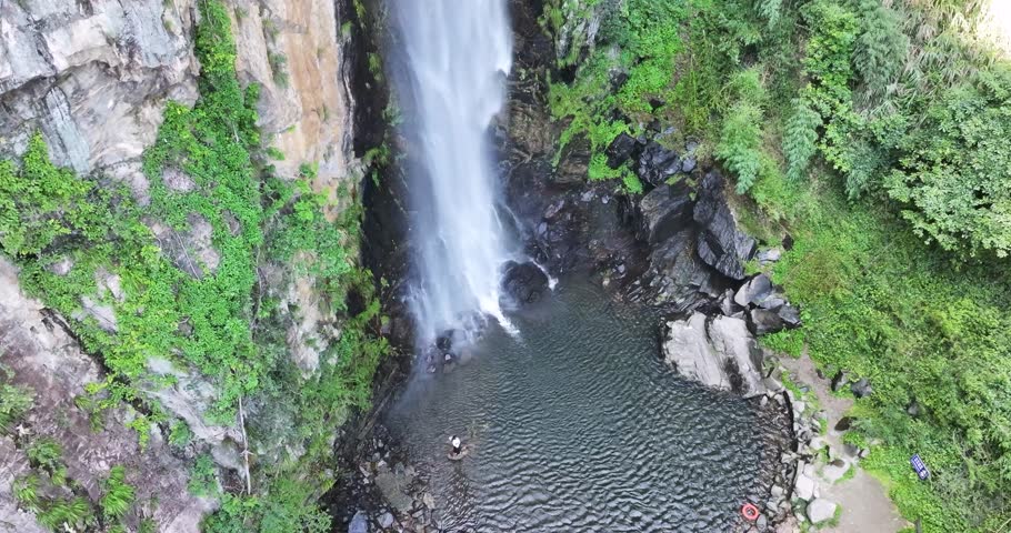 Aerial rising video of Jade Curtain Waterfall (Yu Lian Spring) in Lushan Mountain. A powerful cascade plunges into a serene pool surrounded by lush greenery and rocky cliffs. Jiangxi Province, China.