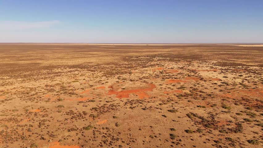 Hay Plains landscape with vast arid terrain, sparse vegetation and red earth stretching to distant horizon, empty arid backdrop, NSW Australia