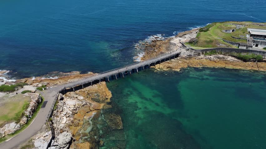 Bare Island Bridge linking the coast with blue ocean and rocky shoreline in Sydney, aerial establishing orbit