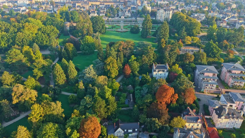 Wide aerial pullback Parc du Thabor with dense tree canopy and autumn colors in Rennes, golden hour establish