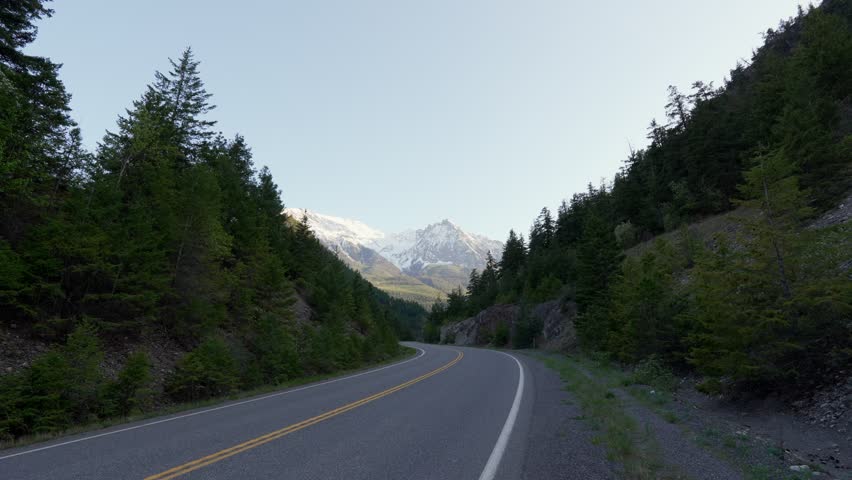 Winding road traversing a mountain pass with evergreen trees and snow capped peaks