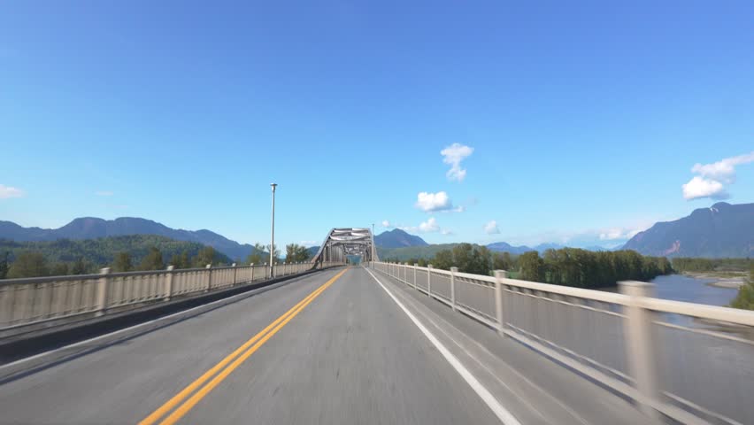 Road view inside a car traveling on a sunny day across a long metal bridge over a river