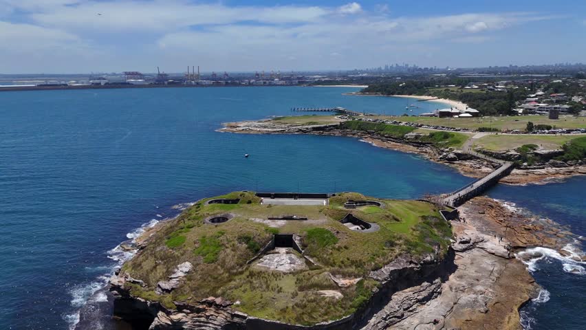 Bare Island causeway with rugged shoreline and open ocean surrounding Sydney, Australia, aerial pullback establish