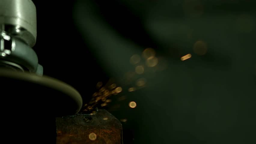 Detailed view of an industrial angle grinder cutting through a piece of rusty metal while producing a stream of bright glowing orange sparks