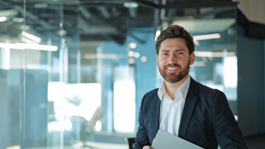 Smiling professional with laptop exudes confidence, success in bright, modern office. Reflects positive corporate attitude and leadership. Portrait of business man indoor