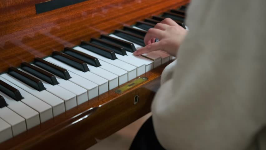 A close-up shot of a girl hands playing the piano during a rehearsal or exam preparation at a music school. Finger placement and the keyboard, learning process and classical music atmosphere.