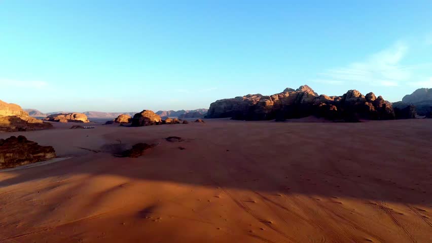 aerial drone sequence sweeping across the red sand valleys of Wadi Rum as the sun sets, casting long shadows over the rock formations