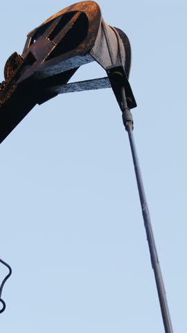Pumpjack pulls bridle to extract fossil fuel at oilfield under blue sky vertical shot. Old equipment pumps crude oil from onshore well closeup