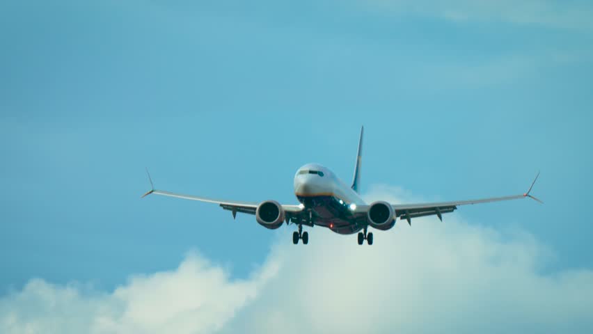 Airliner experiencing strong crosswind with noticeable tilt. Jet adjusting to gusts while flying in partly cloudy sky. Passenger aircraft descending with landing gear down in turbulence. Twin engine