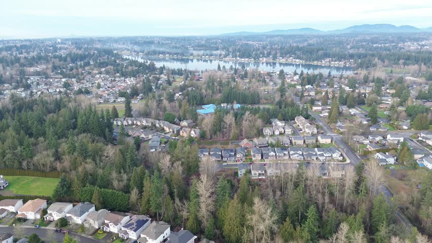 Residential grid extends toward Lake Meridian along East Hill plateau near route connecting Kent to Maple Valley. Shingle patterns, tall conifers, reflective water light layered depth, Kent, WA. USA