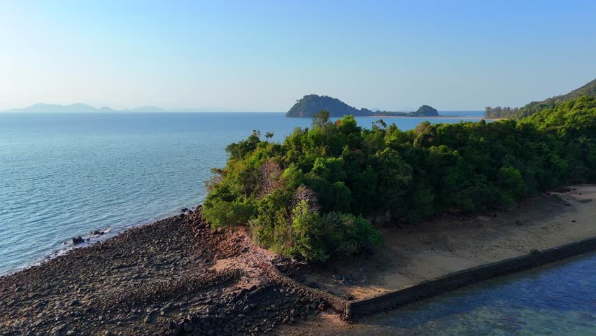 Aerial view of tropical coastline with lush jungle hills, sandy beaches, and clear blue sea surrounding peaceful Koh Phayam island.