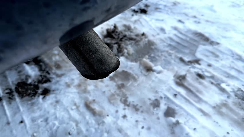 Car exhaust pipe releasing smoke and fumes onto a snowy, dirty ground during a cold winter day
