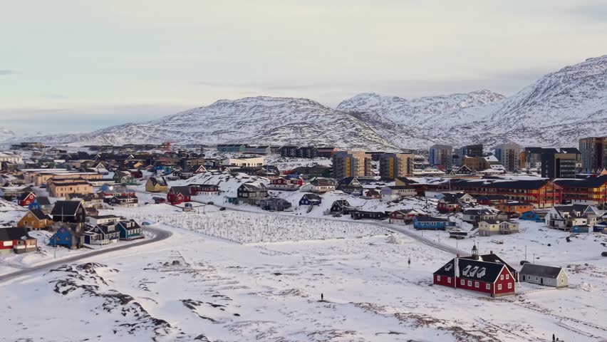 Scenic aerial panorama of Nuuk, Greenland. Featuring iconic colorful Nordic houses, snow-covered streets, and the historic colonial harbor against a backdrop of majestic Arctic mountains.