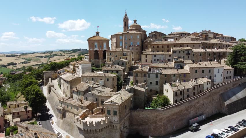 Aerial drone footage of Corinaldo, Italy, a historic hilltop town in the Marche region. Sunny daytime view of medieval walls, rooftops, and surrounding countryside, showcasing traditional Italian architecture and scenic landscape.