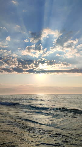 Beautiful seascape. Sea landscape. Ocean scenery. Blue water of calm sea, horizon line, blue sky, white clouds, sun rays shining through clouds. Sunny morning. Sea coast. Natural background Vertical