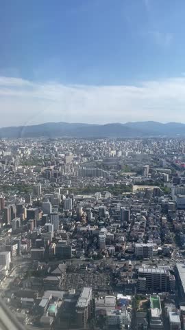 Expansive aerial view of a densely populated city with high-rise buildings, residential complexes, and mountains in the background under a clear blue sky.