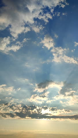 Beautiful landscape. Sky scenery. Calm blue sky, white clouds and sun rays shining through clouds. Sunny morning with sunny beams on sky. Natural background Vertical