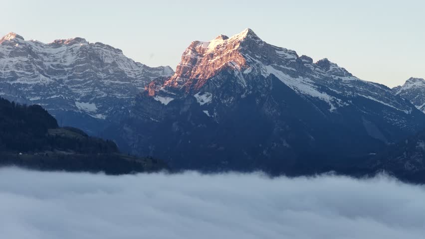 Sunrise light on snowy alpine peaks above fog inversion near Walensee, Switzerland.