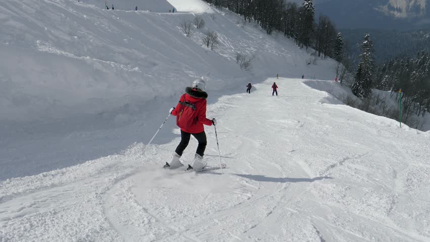 Red skier descending. Sunlit mountain slopes with skier in motion. Dynamic winter sport sequence showcasing skier on snow ridge. Exciting footage of skier skiing down on icy mountain piste