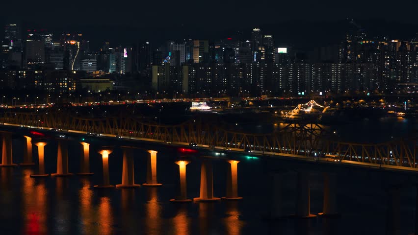 Real-time aerial close-up of a Seoul Metro Line 3 train crossing Dongho Bridge south toward Apgujeong with heavy traffic on Olympic Boulevard and illuminated Gangnam skyscrapers at night