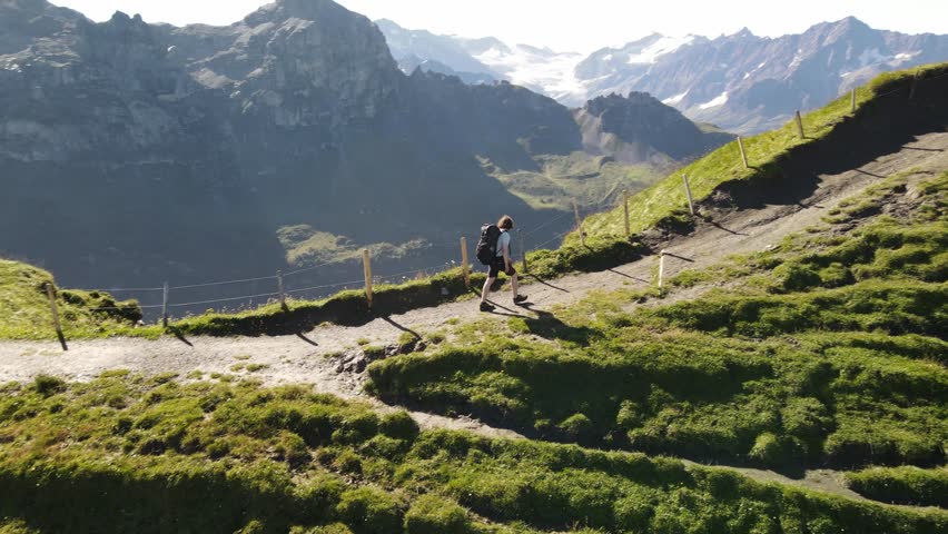 Backpacker hiking along a scenic mountain ridge in the Swiss Alps, high alpine trail with panoramic views, remote wilderness, Via Alpina route, summer hiking adventure Switzerland. Aerial drone view.