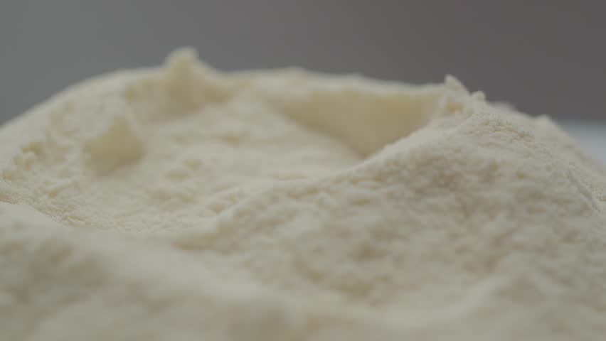 A spoon is shown filling with fine powdered milk, showcasing the textures and details of the milk powder in a kitchen environment.