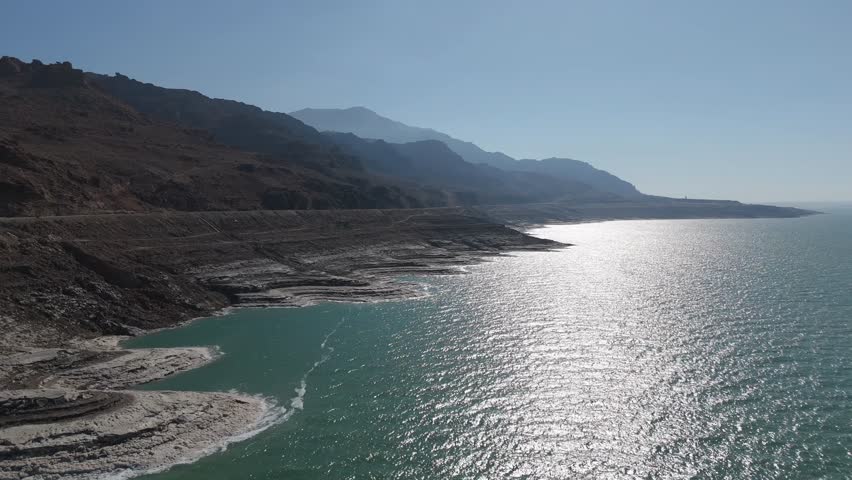 aerial perspective of the Dead Sea shore, featuring vibrant turquoise waters and white salt deposits against the arid Jordanian mountains