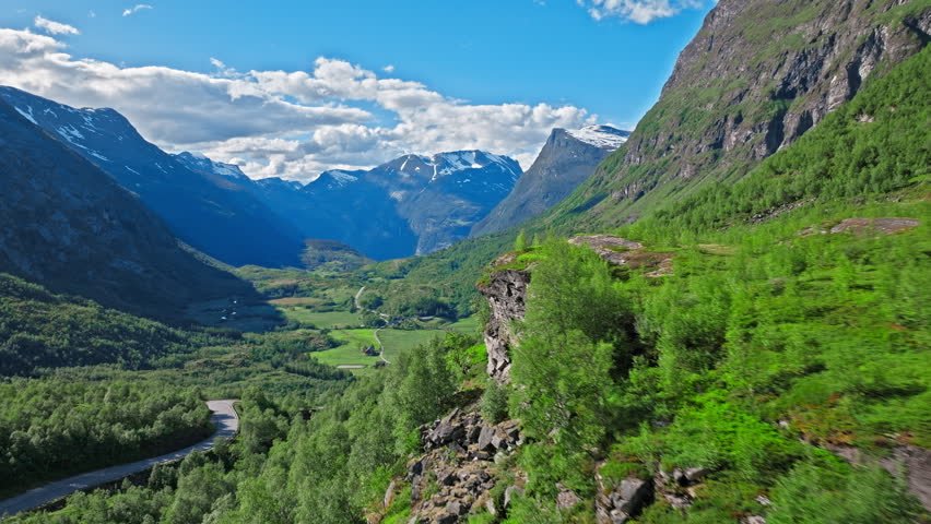 Aerial landscape view in Norway showing a broad Norwegian valley with winding terrain and distant peaks beyond the cabin site. Daylight emphasizes scale and serenity.