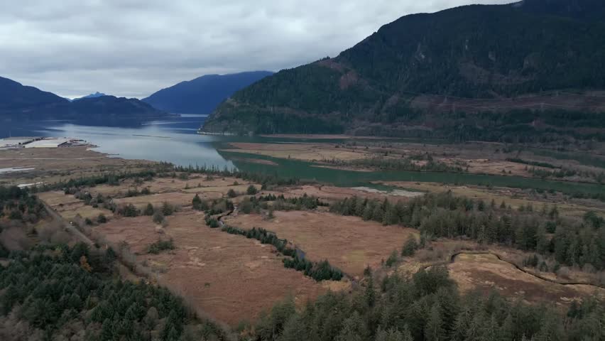 Squamish, Canada - A Winding River Cuts through Open Wetlands, Surrounded by Forested Slopes and Distant Mountains Under a Cloudy Sky - Aerial Drone Shot