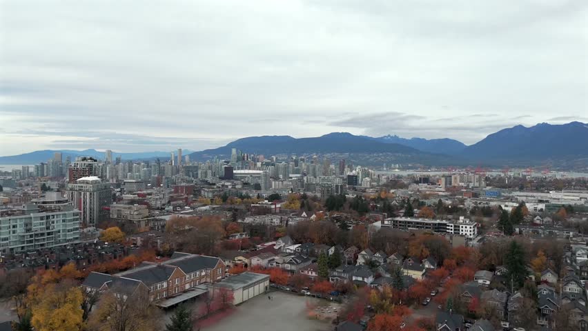 Vancouver, Canada - A Dense City Skyline Rises Behind Colorful Autumn Neighborhoods with Mountains Stretching Across the Distant Horizon - Drone Flying Forward