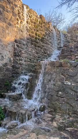 Beautiful cascading waterfall flowing down a rustic stone wall into a stream on a sunny day