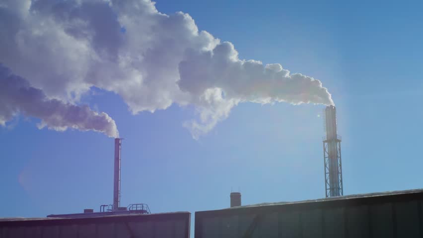 Smoke coming out of two tall factory chimneys against a blue sky. Steam coming out of two chimneys. Air pollution. Contrast.