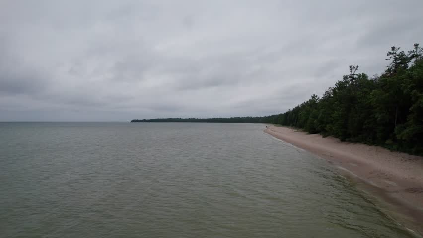 Drone shot low next to trees and towards beach.  Northern Door County Wisconsin in the summer time.  Lake Michigan waves lap against the shoreline.
