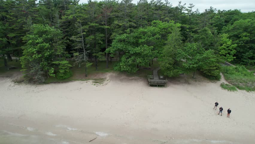 Right to left rising Drone shot of Northern Door County Wisconsin on summer overcast day.  Tree lined beach.