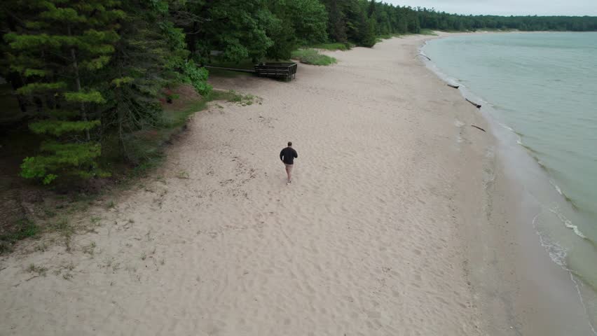 Follow drone shot of man on beach in Northern Door County Wisconsin.  Lake Michigan water a tree lined shore.