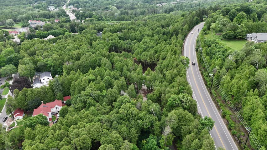 Aerial of Fish Creek in Door County Wisconsin on an overcast day. Drone push shot over road with cars and hilly terrain in the distance.