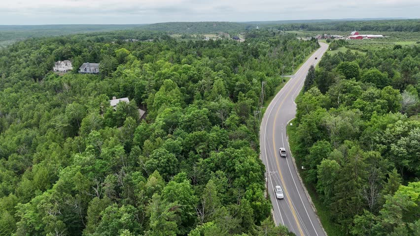 Aerial of Fish Creek in Door County Wisconsin on an overcast day.  Drone push shot over road with cars and hilly terrain in the distance.