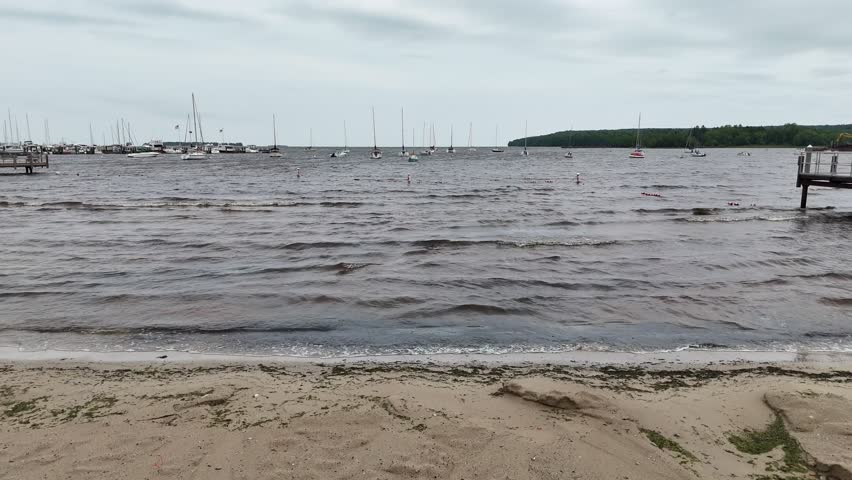 Aerial of Fish Creek in Door County Wisconsin on an overcast day.  Low drone approach shot from beach over water.  Rising over sailboats in the bay.