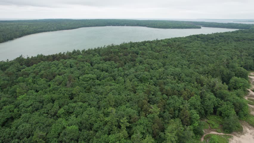 Push Drone shot of Europe Lake in Northern Door County Wisconsin on summer overcast day.  Tree lined Calm Water.