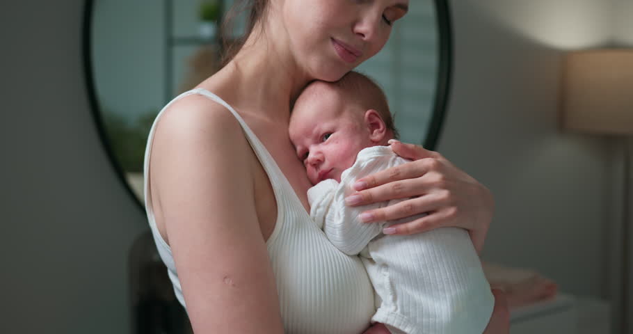 Mother cradles her newborn baby in her arms, showing tender affection and maternal love in a gentle embrace