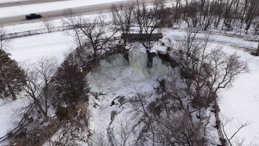 Aerial Birdseye shot of Frozen Waterfall in Green Bay Wisconsin. Narrow river leading up to bridge and falls.