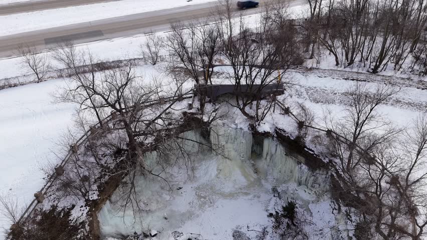 Aerial nosedive shot of Frozen Waterfall in Green Bay Wisconsin.  Revealing River and snow below, with bridge.