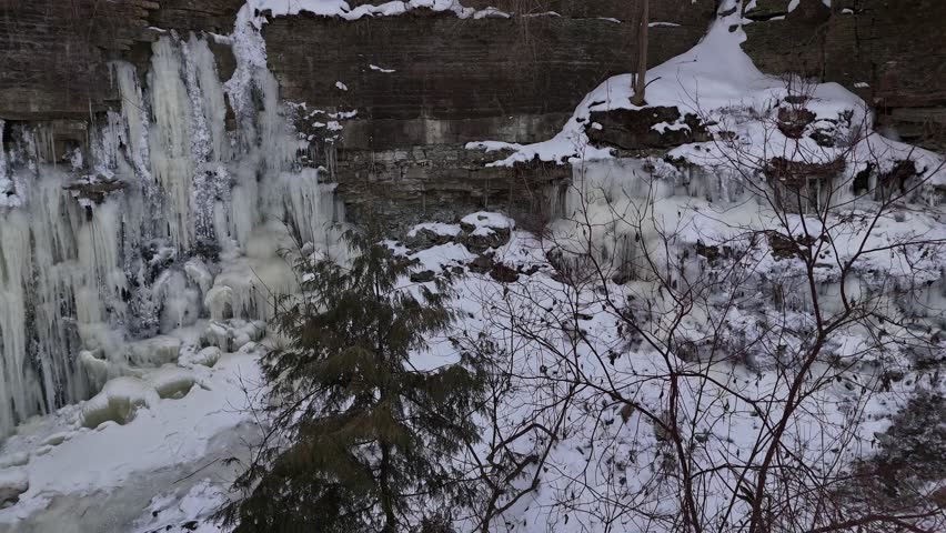 Aerial Pull shot of Frozen Waterfall in Green Bay Wisconsin.  Ice, snow and tree branches over river.