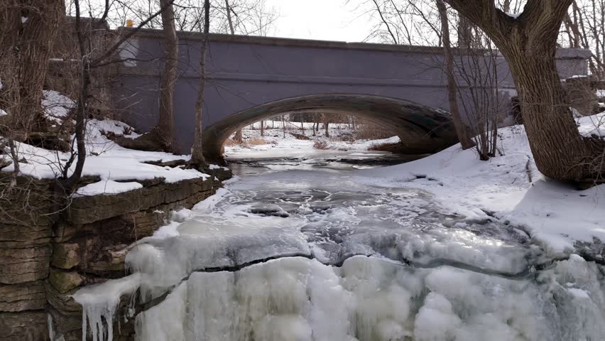 Aerial Push shot of Frozen Waterfall in Green Bay Wisconsin.  Ice, snow and tree branches over river.