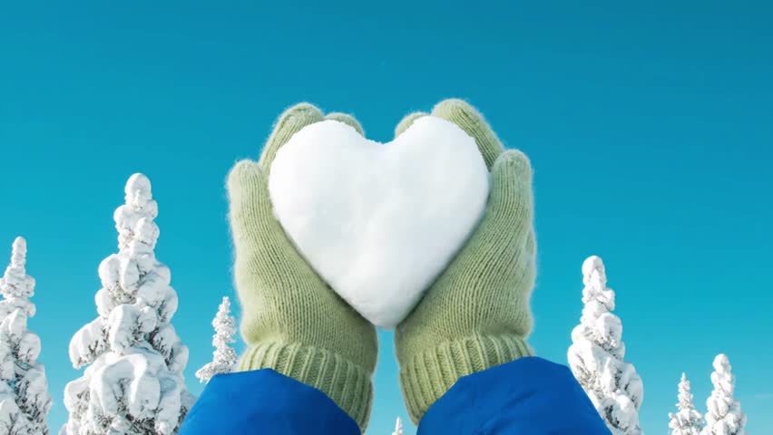 Hands in winter gloves holding a heart shaped snowball against a snowy background