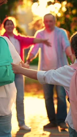 Children run with backpacks to mom dad, hug parents on street. Family mom dad, children in city park. Parents pick up daughters from school. Happy family. Concept of education. Children's education