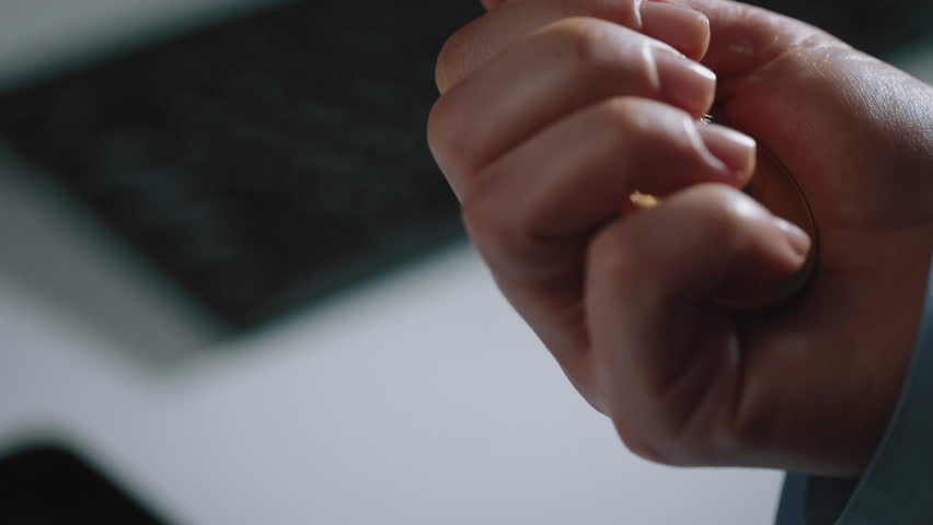 A close-up of a hand holding several Bitcoin coins, showcasing the digital currency in an office environment. The background features a blurred keyboard, emphasizing the business context.