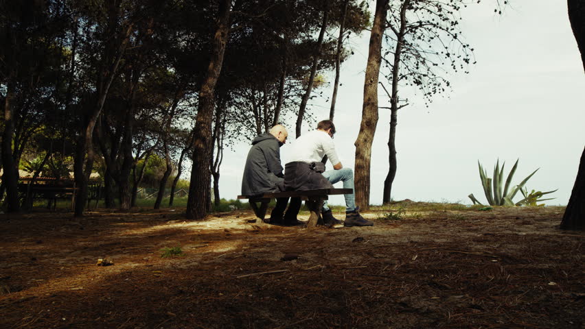 Two Men Sitting on a Bench Watching the View Below a Forest